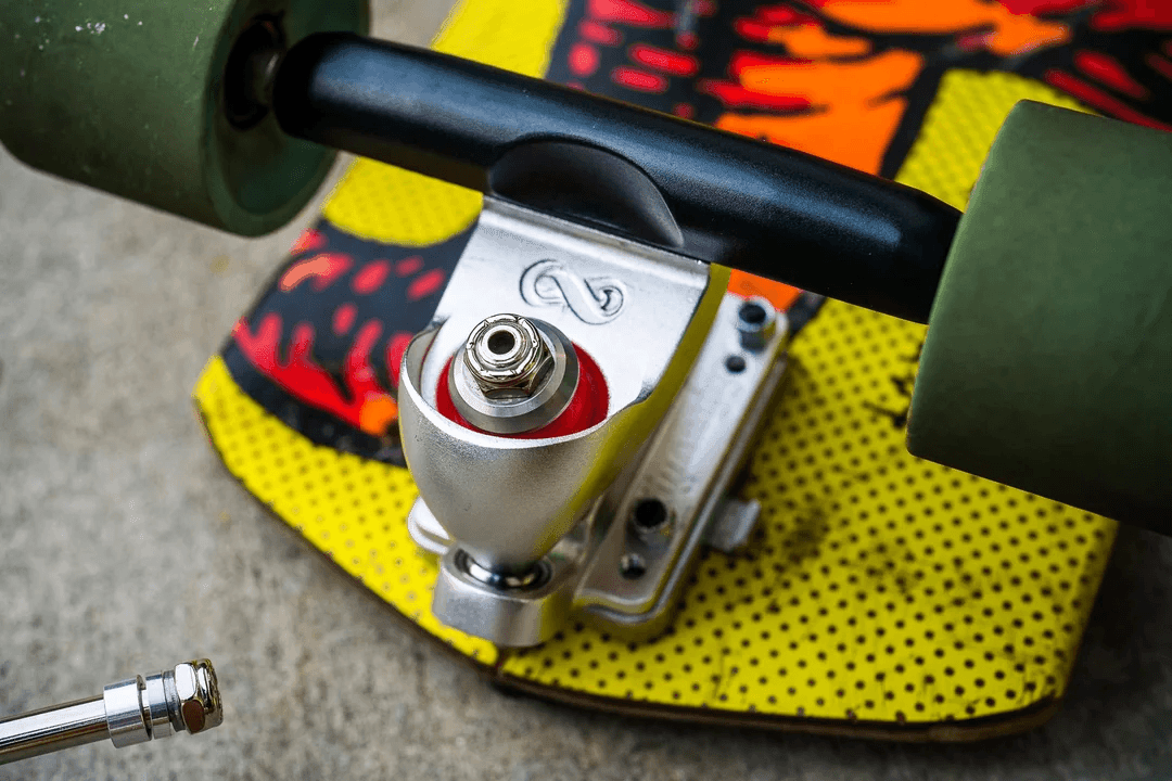 Close-up of a skateboard truck with green wheels and a colorful deck on concrete.